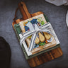 Charcuterie recipe cards tied with a ribbon on a wooden cutting board and towel; finished with cheese tool set