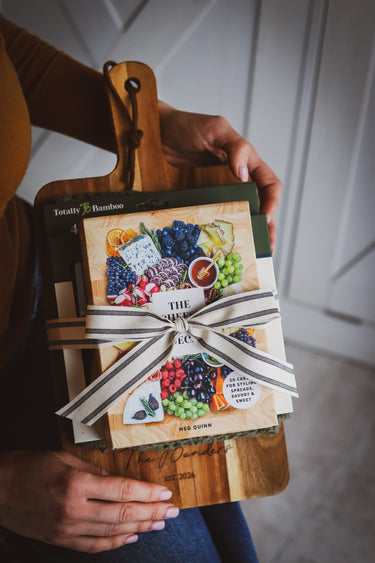 Person holding a book wrapped in ribbon on a wooden cutting board.