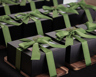 Black gift boxes with green ribbons on a wooden cutting board