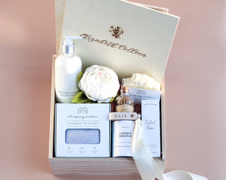 A gift box open to reveal various products including a candle, a soy sauce bottle, a box of matches, a keychain, a basket with dry flowers, and several other lavender-themed items.