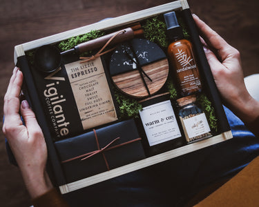 Luxury gift set with coffee products, candle, coasters and a bottle of sandalwood room spray held by a person.