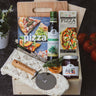 Wooden cutting board with pizza ingredients and a cookbook on a dark surface.