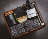 Gift set with bottle labeled 'Savon Blanc', black mug, wooden coaster, and patterned towel in a wooden box.