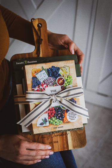 Person holding a custom engraved cutting board with cheese tools and charcuterie recipe cards