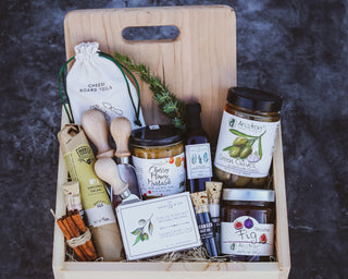 A handmade premium pine wood box containing a curated selection of gourmet food items including crackers, salami, fig preserve, olives, honey mustard, salt set, and cheese board tools.